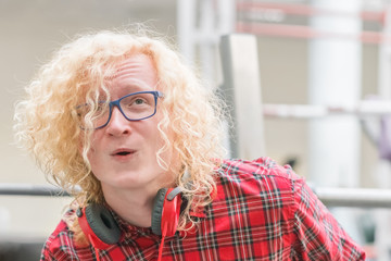 Curly blonde guy with glasses and in a red shirt trains in a gym with a strained face