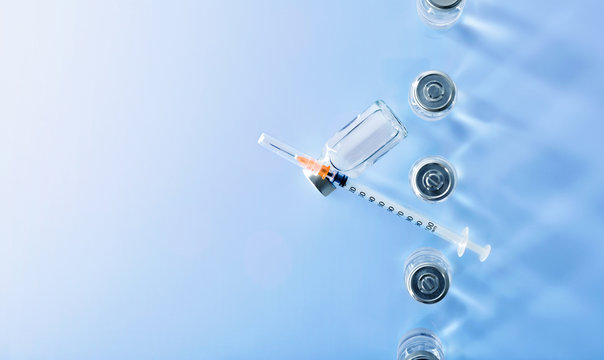 Row Of Vials And Syringe On Blue Table Top View