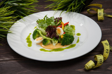 salad greens of cabbage broccoli, pumpkin puree, and quail eggs on a wooden black table, and a centimeter ribbon, healthy food, fitness menu