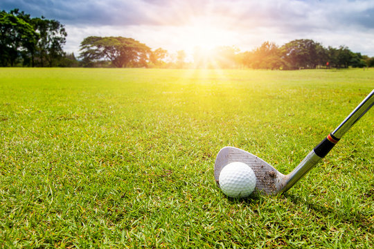 Golf club and golf ball in grass in sunrise.