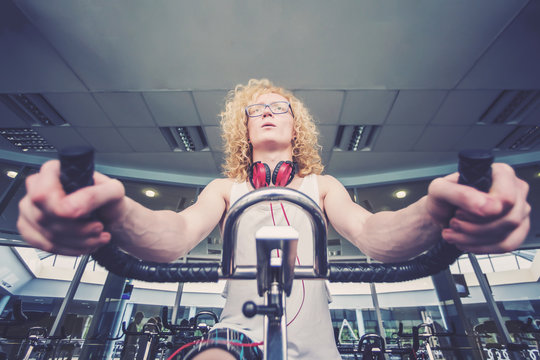 Thin blond man with glasses and red headphones training on a stationary bike