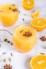 Fall, winter cocktails, Hot and spicy winter orange punch with cinnamon, anise stars, cardamom, cloves. On a white marble table, with ingredients, in glasses. Copy space