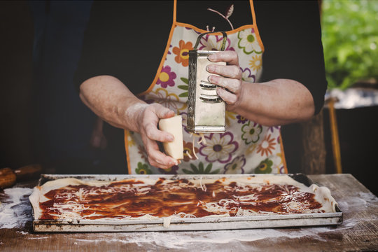 Hands of old woman grating cheese on pizza