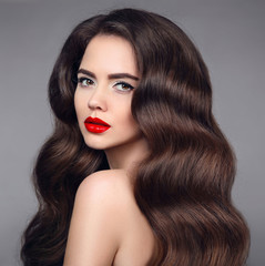 Obraz premium Beauty hair. Brunette girl portrait with red lipstick and long shiny wavy hair. Beautiful model with healthy hairstyle isolated on studio dark background.