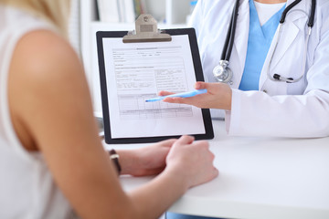 Close up of a doctor and  patient hands while phisician pointing into medical history form at clipboard