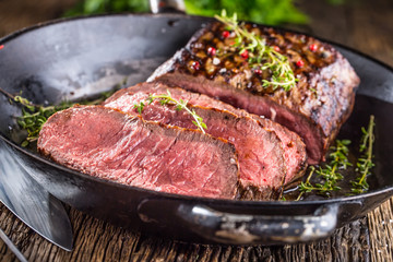 Beef steak. Juicy medium Rib Eye steak slices in pan on wooden board with fork and knife herbs spices and salt