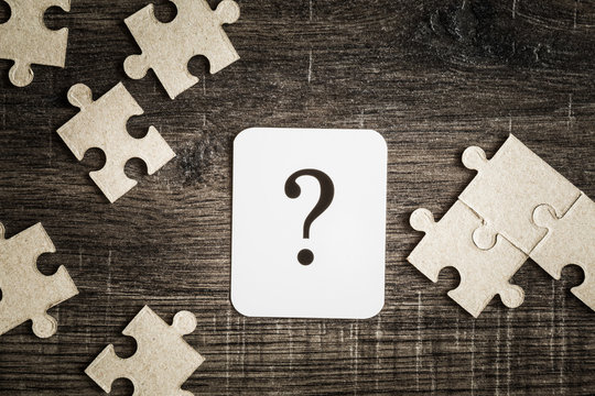Sign of question with puzzle on the wooden background. Solution search concept. 