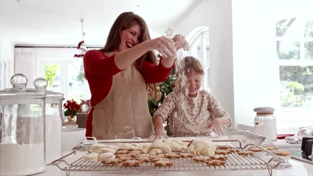 Smiling mother and daughter playing with cookie flour at kitchen counter while making Christmas cookies. Baked cookies and muffins on tray for Christmas eve.
