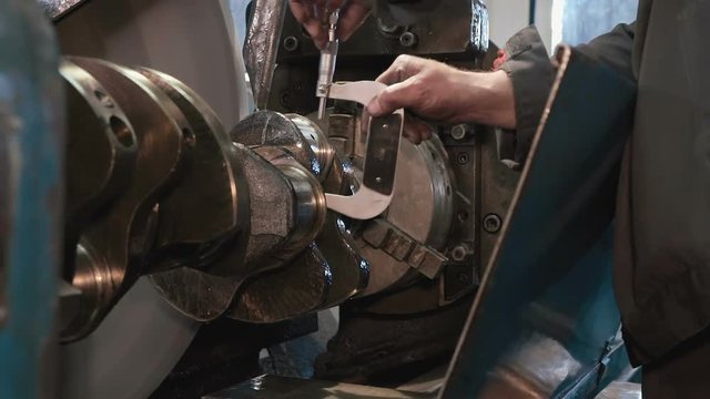 Close up of man hands checking micrometer reading after grinding crankshaft, cooling emulsion flows. Shot with Sony a7s and Atomos Ninja Flame in shabby car service.