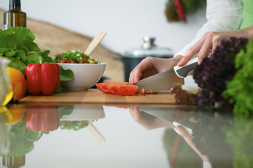 Closeup of human hands cooking vegetables salad in kitchen on the glass  table with reflection