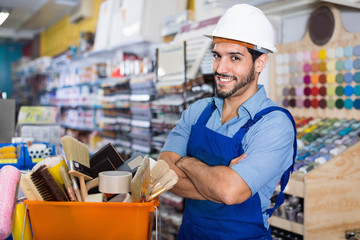 Workman standing folded arms near basket with picked tools in paint store