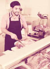 Obraz premium Adult man butcher is cutting meat for client