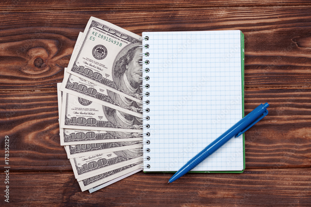Poster notebook with ballpoint pen and dollar banknotes on a wooden table