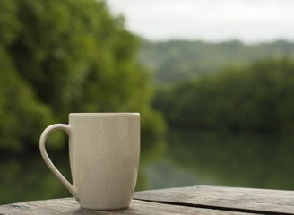 coffee cup / A white cup of coffee is placed on the floor of an old wooden table with a natural backdrop and a blur.