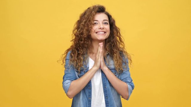 Happy curly woman in denim shirt rejoice while moving her head and looking at the camera over yellow background