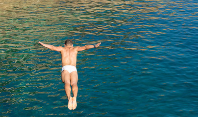 Cliff diver guy jumping in the blue sea from high rocks wall - Joyful freedom concept and carefree sensation feeling the pure connection with the nature - Natural vivid afternoon color tones