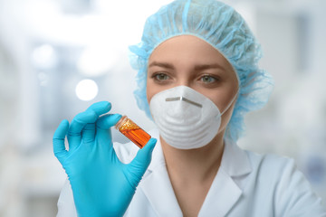 Female scientist or tech in lab coat, gloves and hat holds liquid biological sample