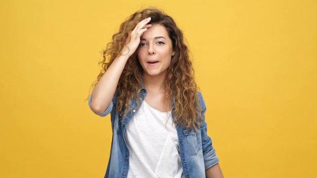 Happy Carefree Curly Woman In Denim Shirt Dancing And Looking At The Camera Over Yellow Background