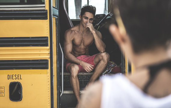 Young man sitting on steps of school bus looking at young woman