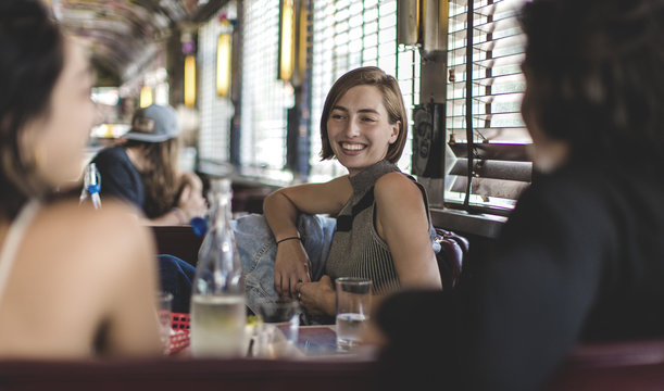 Smiling woman sitting with two friends in a booth in a diner.