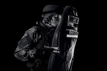 Armed with a pistol, a military man in a bulletproof vest covers himself with a shield