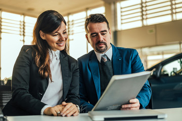 Happy woman with car dealer in auto salon looking at documents.