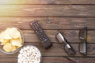 popcorn, chips in a glass bowl, TV remote control, stereo glasses on a wooden background, leisure, watching a movie, a match