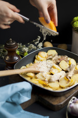 fried potatoes with mushrooms and cheese, in a frying pan, on a black background