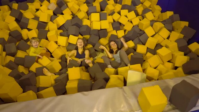 Two young women and a boy having fun with soft blocks at indoor children playground in the foam rubber pit in the trampoline center.