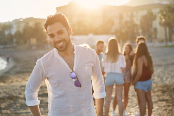Handsome young man standing on beach with friends smiling