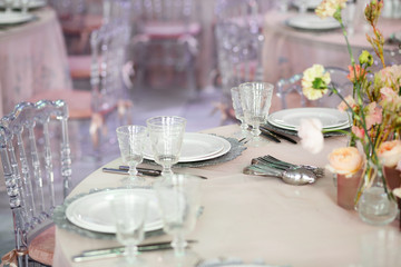 Silver flatware, white plates and crystal glasses on pink dinner table