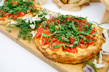 Pizza with many tomatoes and greenery served on wooden board