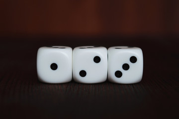 Three white plastic dices in a row on brown wooden board background. Six sides cube with black dots. Start number 123.
