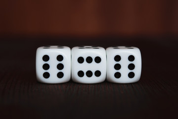 Three white plastic dices in a row on brown wooden board background. Six sides cube with black dots. Devil number 666.