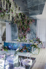 Violet flowers and greenery hang from the wall over white dinner hall