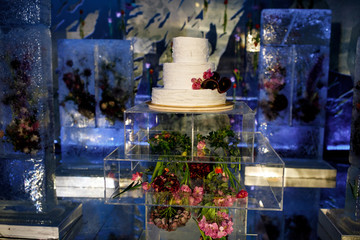 White wedding cake stands on glass box with pink and red flowers