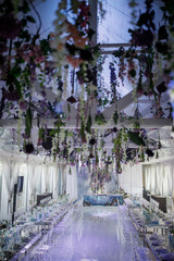 Violet flowers and greenery hang from the wall over white dinner hall