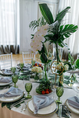 Centerpieces made of large green leaves and white flowers stand on dinner tables in the restaurant