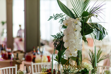 Centerpieces made of large green leaves and white flowers stand on dinner tables in the restaurant