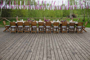 Dinner table served with candles and violet lilac stands on wooden porch