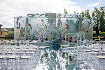 Ice cubes with violet flowers inside  stand before transparent plastic chairs ready for wedding ceremony