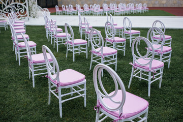 White chairs with pink seats stand on the green lawn before wedding altar