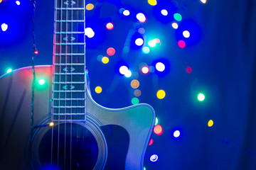 Obraz premium Yellow acoustic guitar with New Year or Christmass garlands on a blue background. Celebrating atmosphere.