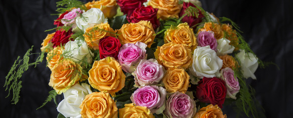 A beautiful and colorful bouquet of big roses in different colors in white paper with a black velvet background
