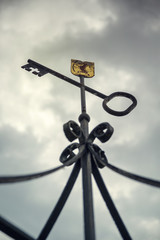 Fototapeta na wymiar Forged cast iron key on a metal bow with a golden label with a dark sky in the background.