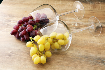 Wineglasses with white grapes and red grapes on wooden background.