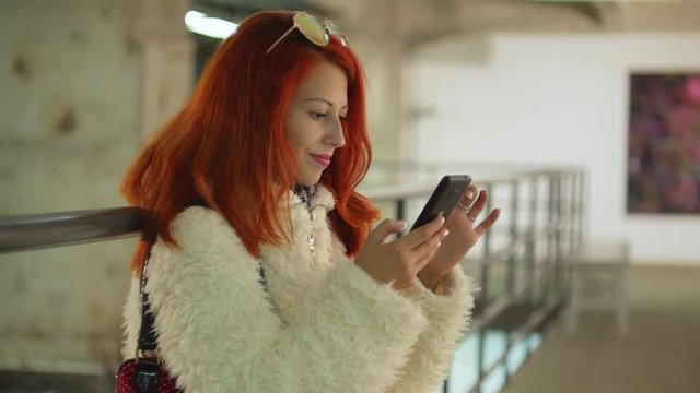 Red hair young woman with mobile at art gallery
