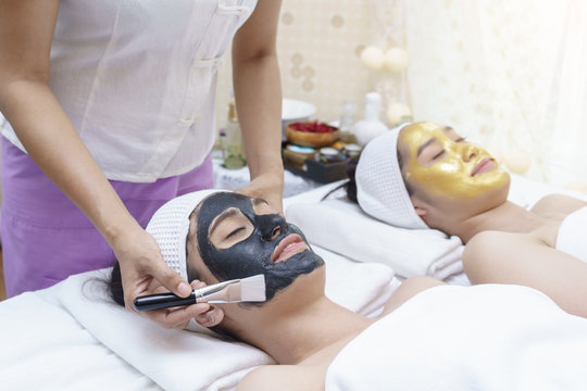 Beautiful smiling young Asian women having mud mask and high quality authentic pure gold facial mask  , lying on massage table in spa salon