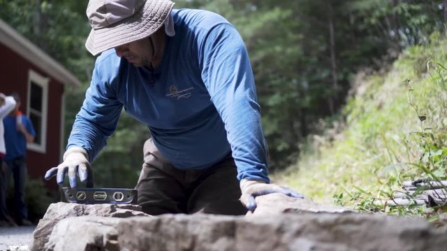 Job foreman checks level on a large rock placed into position under the hot sun.