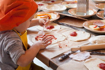 chłopiec robi domowej roboty pizzę pracującą w kuchni w mundurach szefów kuchni i rozmazuje sos bazy - 178370176